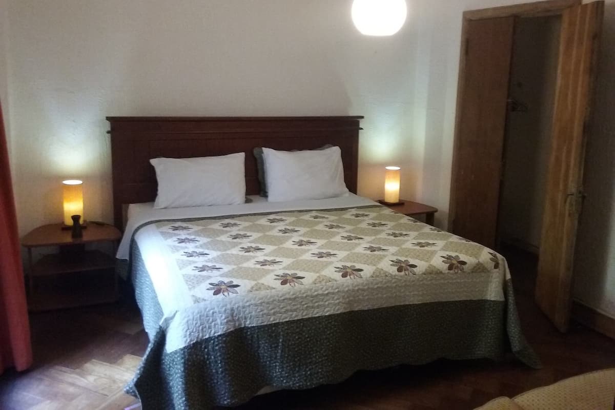 A bedroom with a wooden headboard, two bedside lamps, a floral bedspread, and a wooden door.
