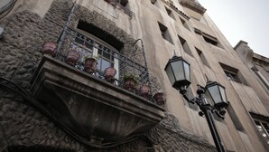 A building facade with a stone base, a balcony with potted plants, and a traditional street lamp. - Hostal ByBSiglo (Santiago)