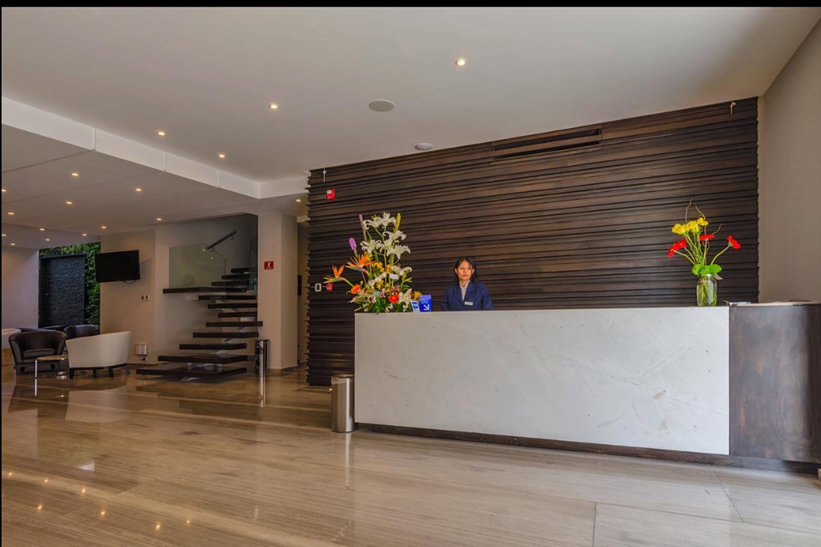 Un área de recepción moderna con una recepcionista, un mostrador de recepción y una escalera.
