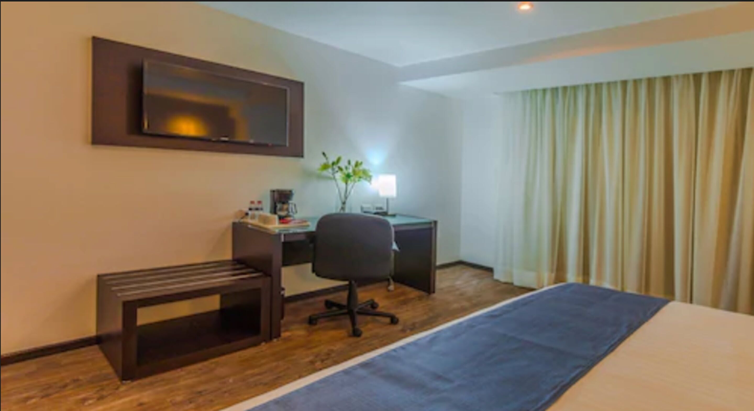 A hotel room with a bed, desk, chair, and a television on the wall.