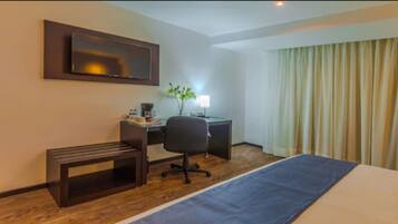 Habitación de hotel con cama, escritorio, silla y televisión en la pared.