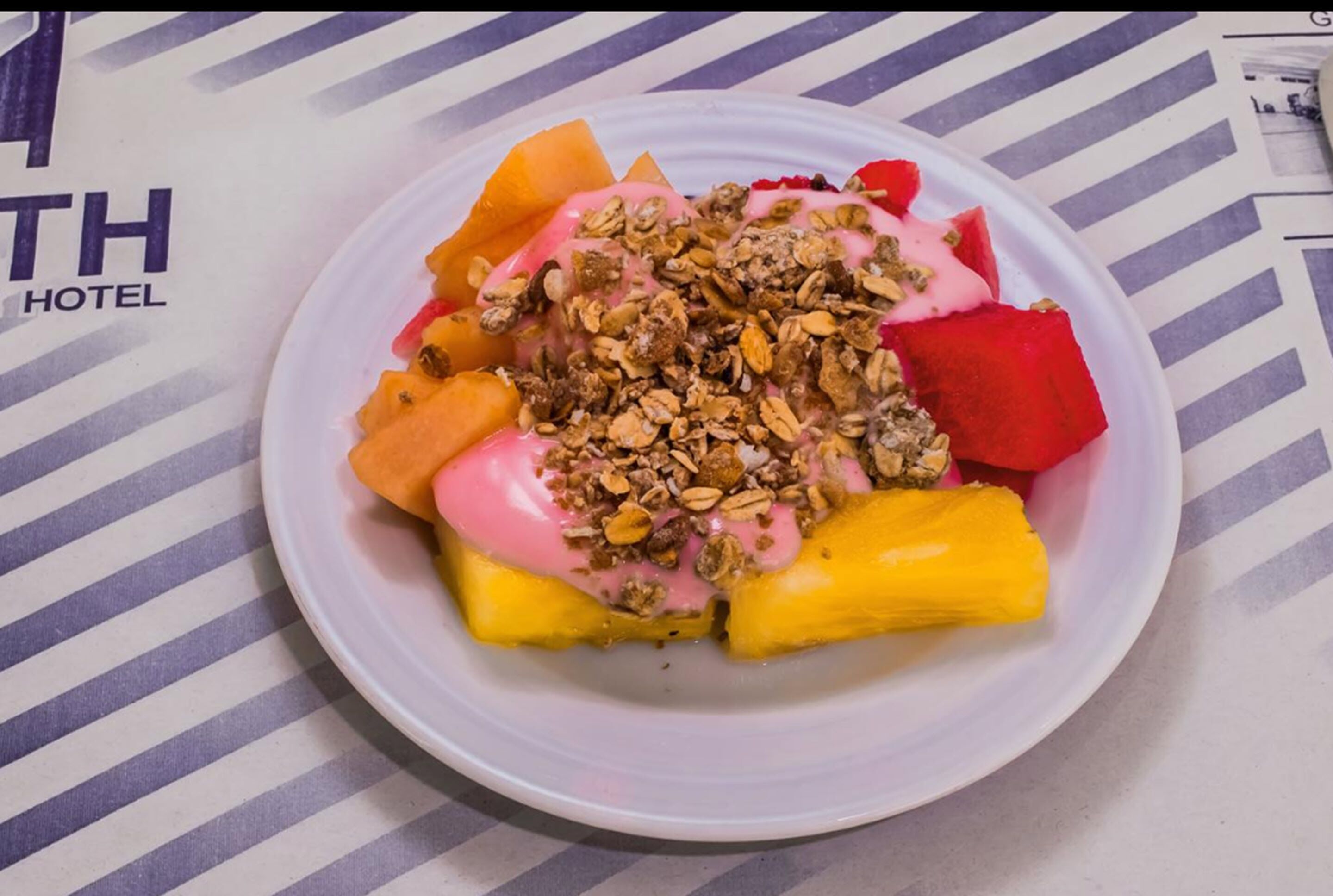 A plate of fruit salad with granola and yogurt on a striped tablecloth.