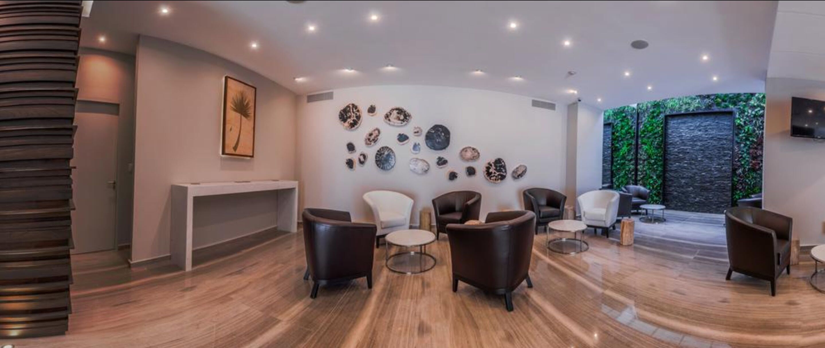 A modern interior with a wooden floor, a reception desk, and a wall decorated with various objects. There are several chairs and a sofa arranged for seating.