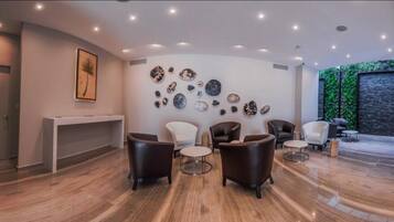 A modern interior with a wooden floor, a reception desk, and a wall decorated with various objects. There are several chairs and a sofa arranged for seating.
