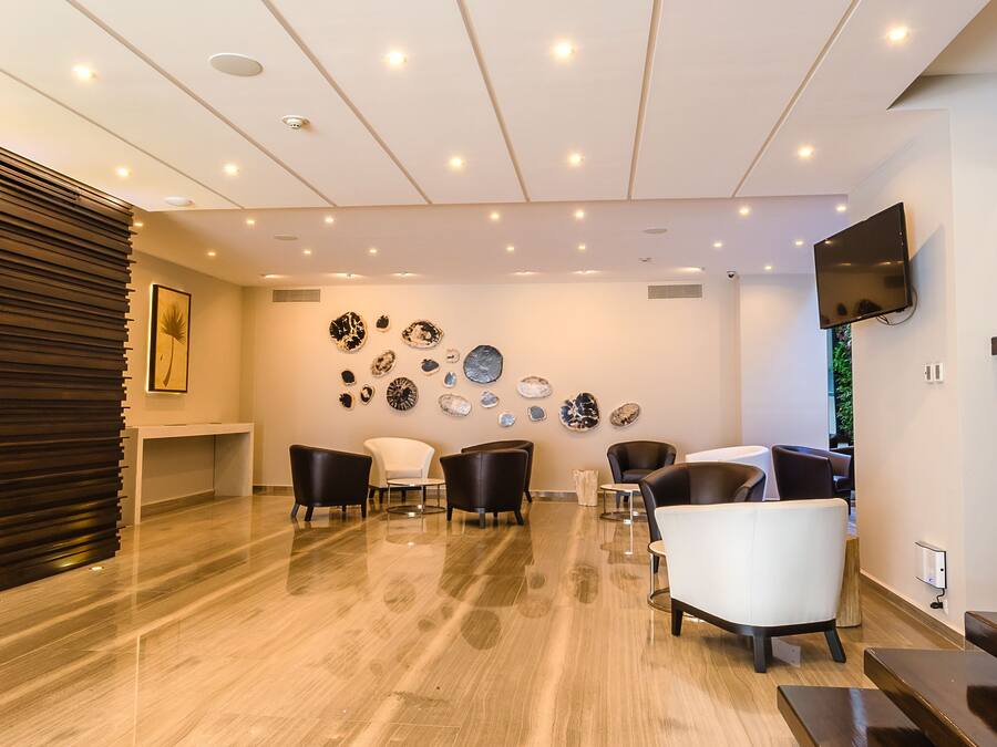 Eine moderne Hotelhalle mit poliertem Marmorboden, einer Rezeption, mehreren Sitzbereichen und einem an der Wand befestigten Fernseher.