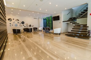 A modern lobby with a polished marble floor, a staircase with glass railings, and a wall adorned with various decorative plates.