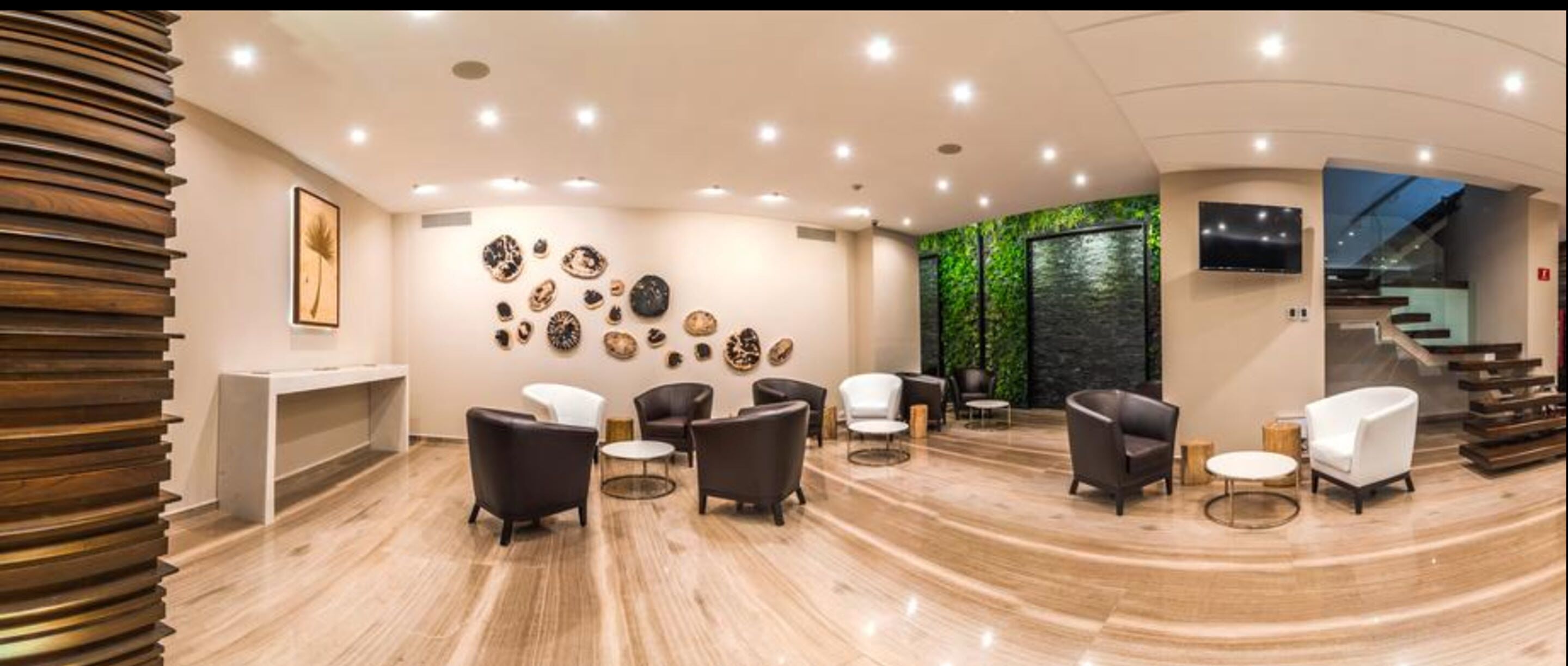 Un intérieur moderne avec un espace salon aux lignes courbes, un téléviseur fixé au mur et un escalier.