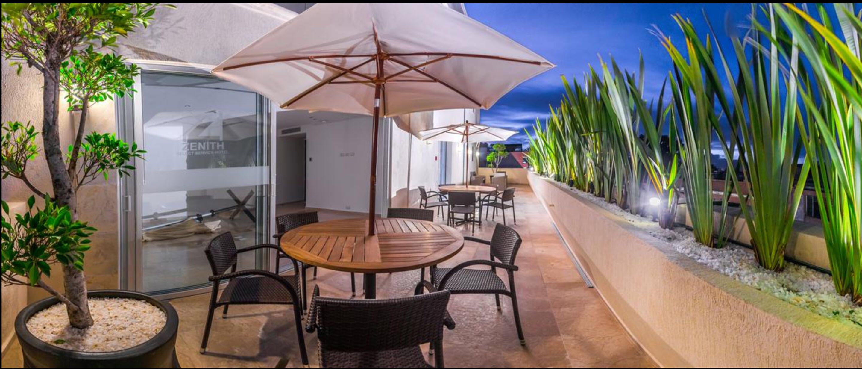 Eine Terrasse im Freien mit einem runden Holztisch und Stühlen, umgeben von Sonnenschirmen.