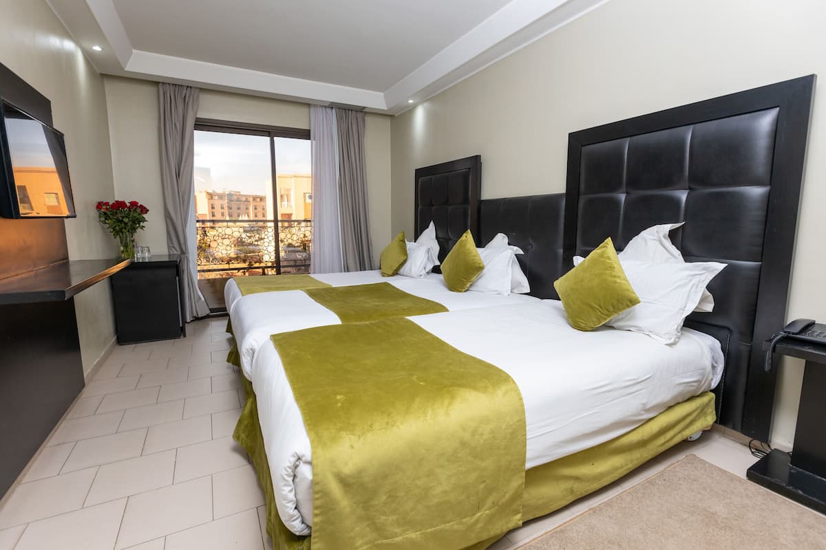 A hotel room with a large bed, a TV, a desk, and a view of the city through the window.