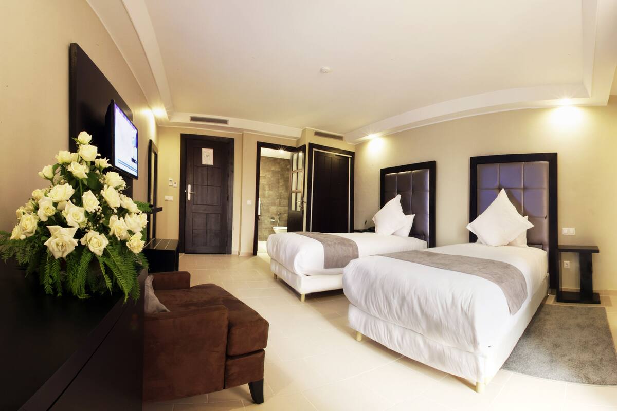 A hotel room with two beds, a TV, a desk, and a large bouquet of white flowers.