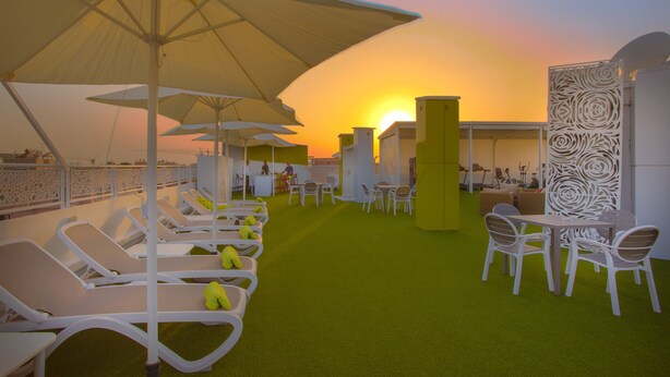 A rooftop lounge with sun loungers, umbrellas, and a green carpeted area.