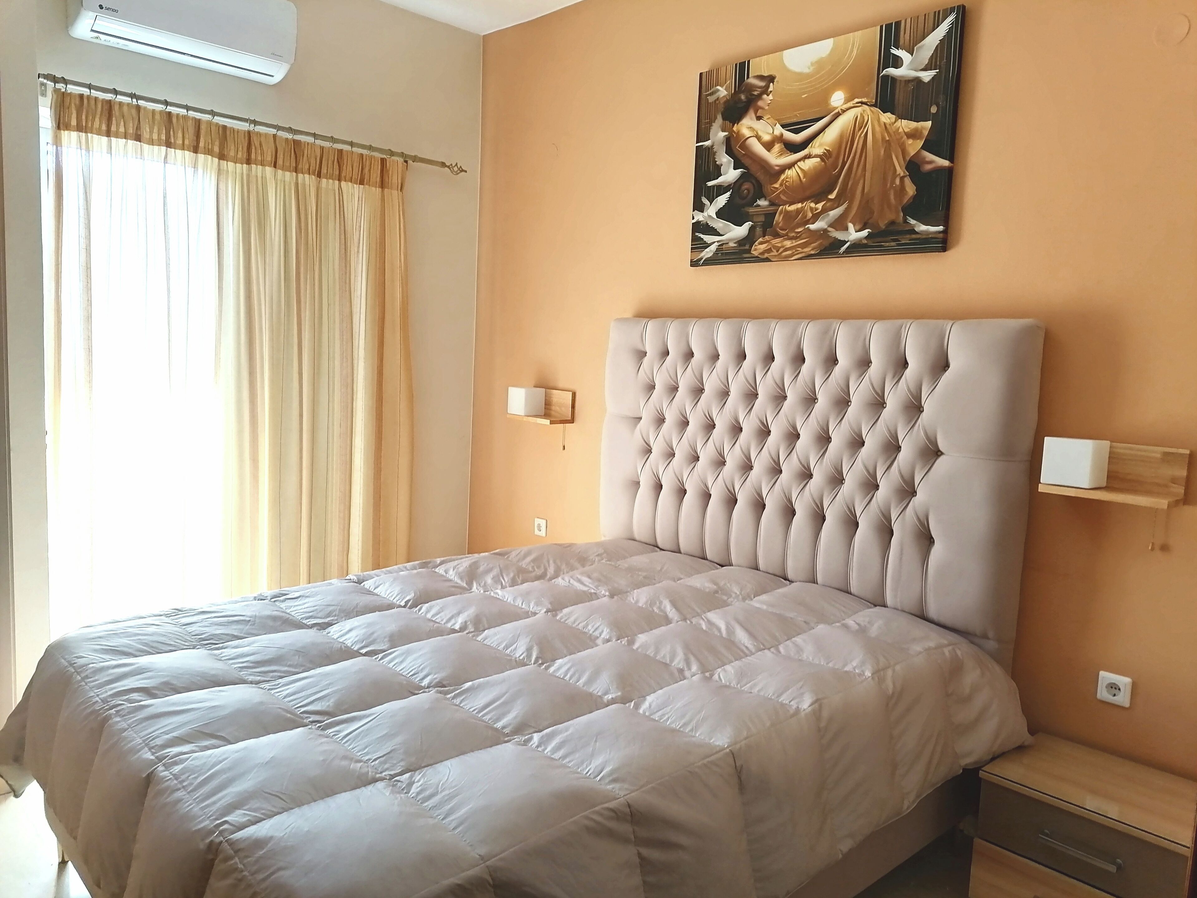 Un dormitorio con una cama grande, cabecera, un cuadro y una mesita de noche.