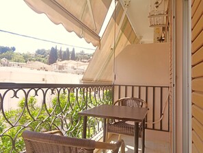 A balcony with a table and two wicker chairs, overlooking a residential area with houses and trees. - Villa Maria (Parga)