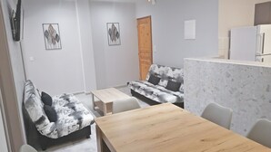 A modern living room with a sofa, a wooden table, and a kitchen area. - Villa Maria (Parga)