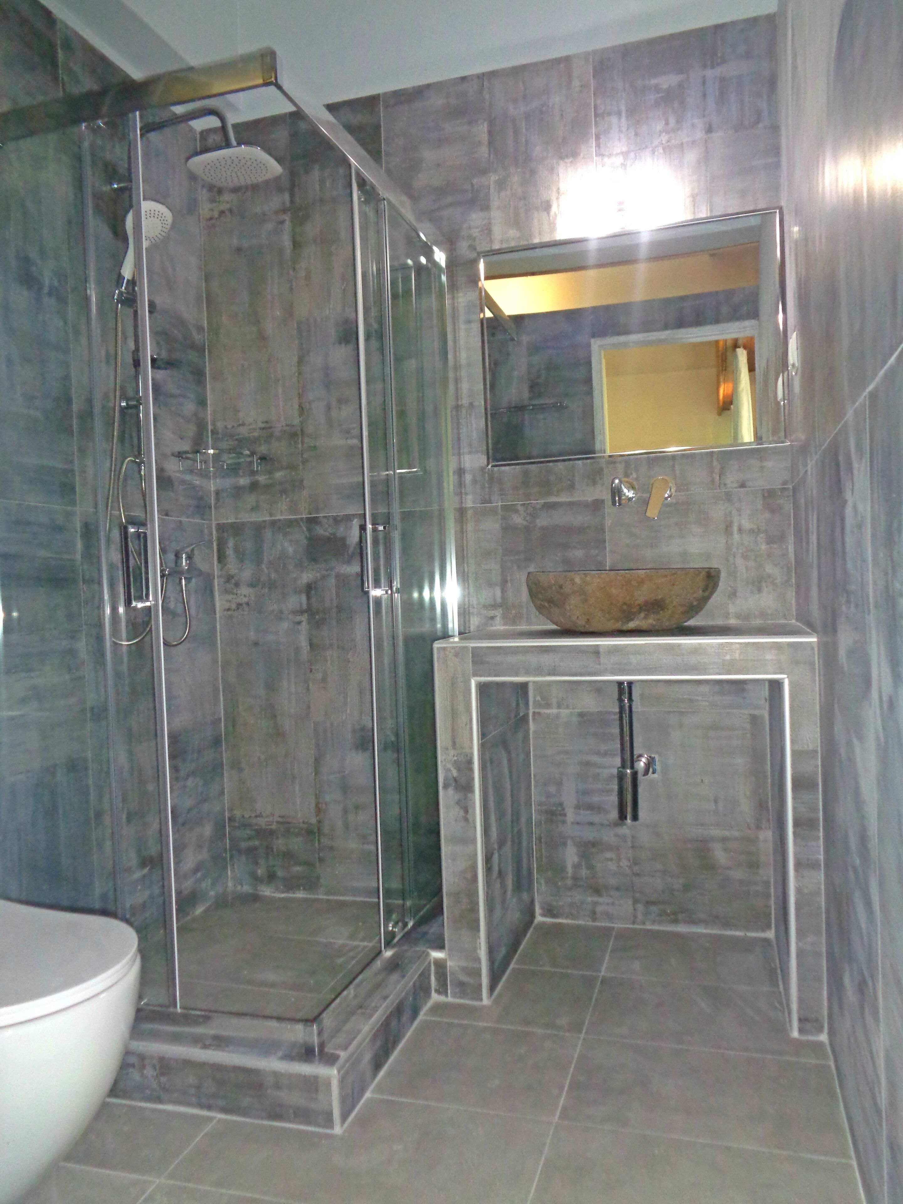 A modern bathroom with a glass-enclosed shower, a marble sink, and a large mirror above it.