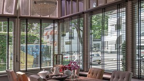 Un comedor con una mesa y sillas de madera, ventanas amplias con persianas y una lámpara decorativa.