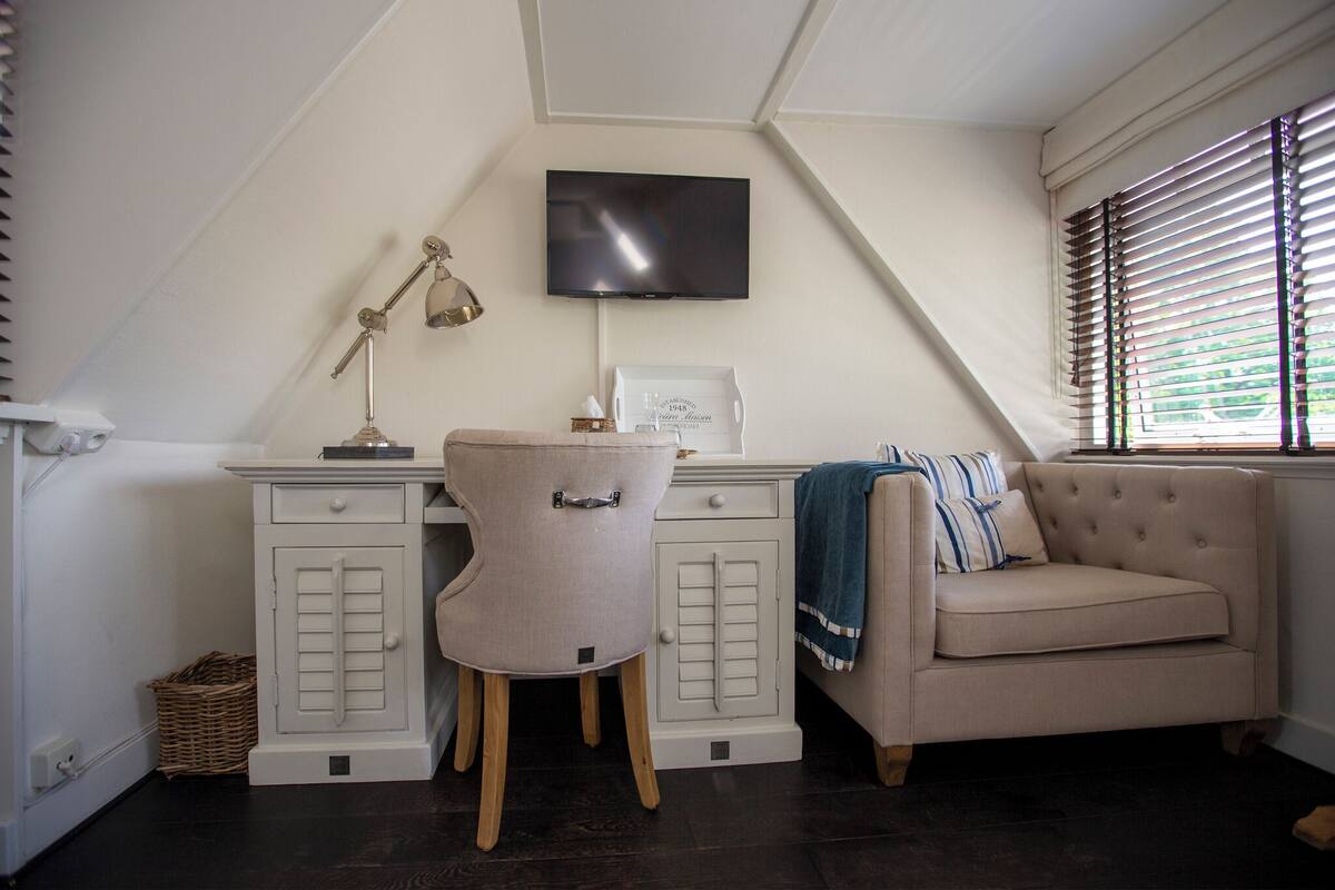 A room with a desk, chair, television, and a sofa.