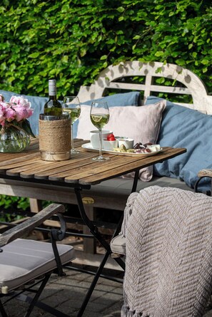 A wooden table set with a bottle of wine, glasses, and a plate of food, with a wicker basket and a vase of flowers. - Zenzez Hotel & Lounge (Apeldoorn)