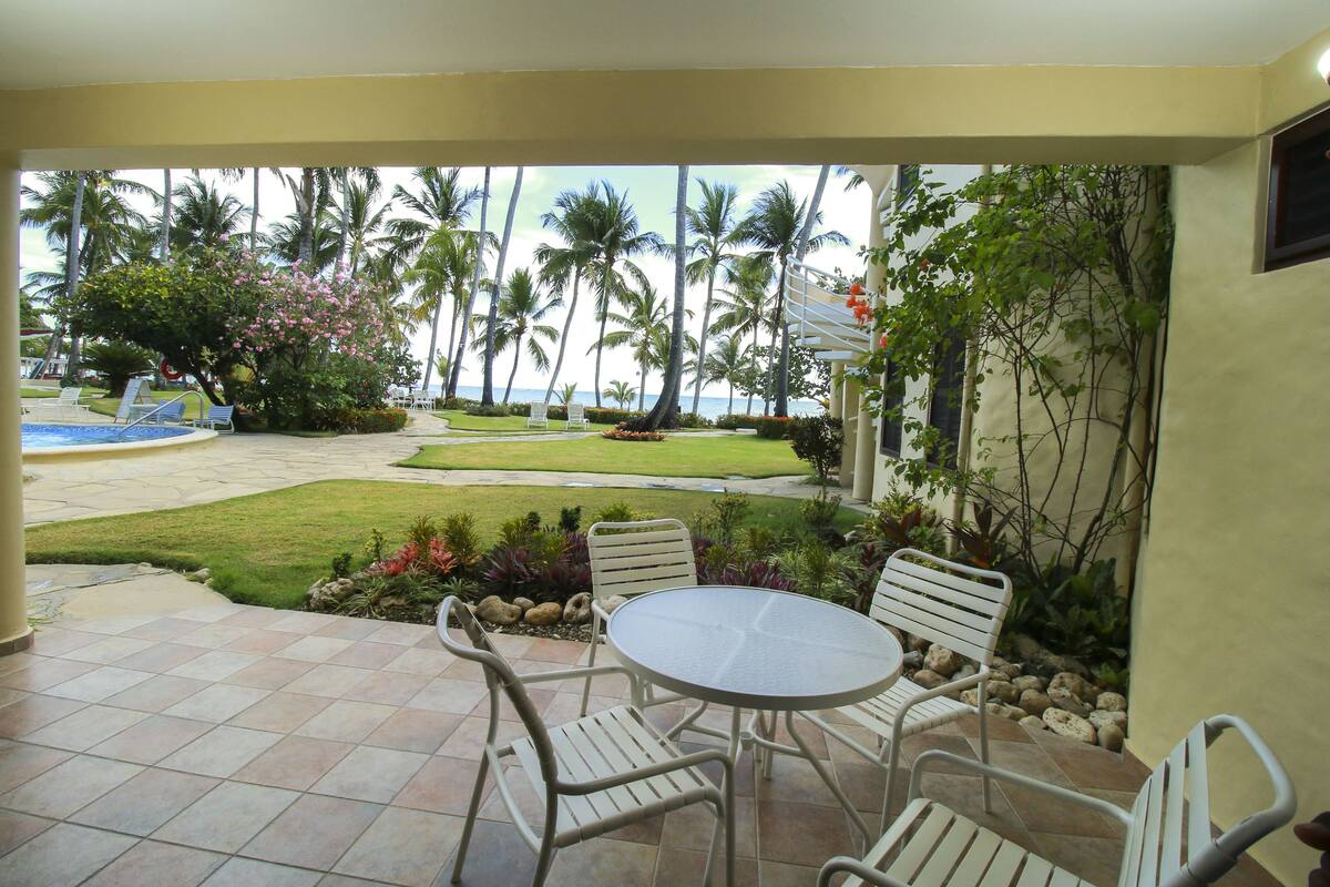 A patio with a round table and four chairs, overlooking a pool and palm trees.