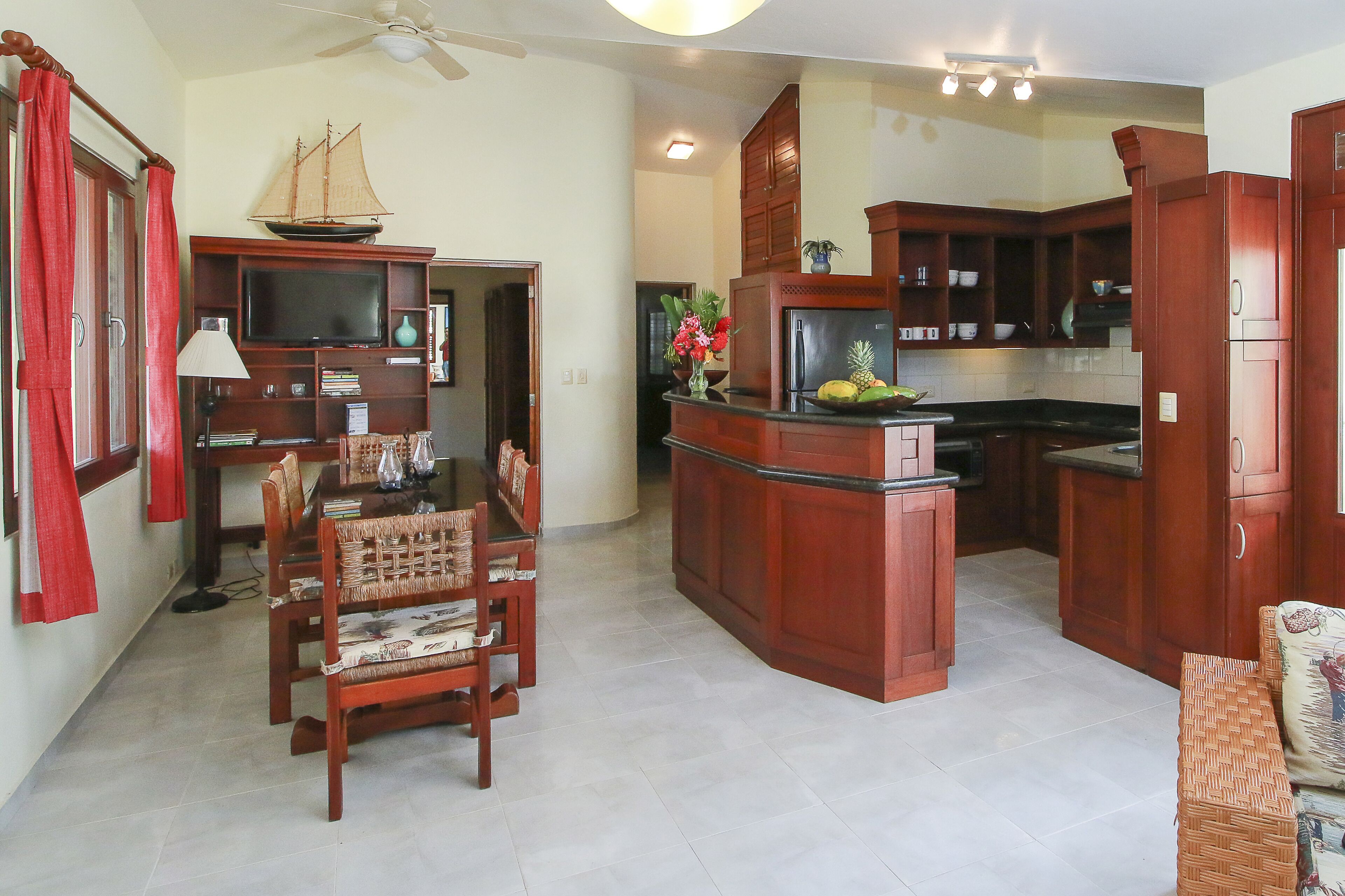 A spacious living area with a dining table, chairs, and a kitchen with wooden cabinets and a refrigerator.
