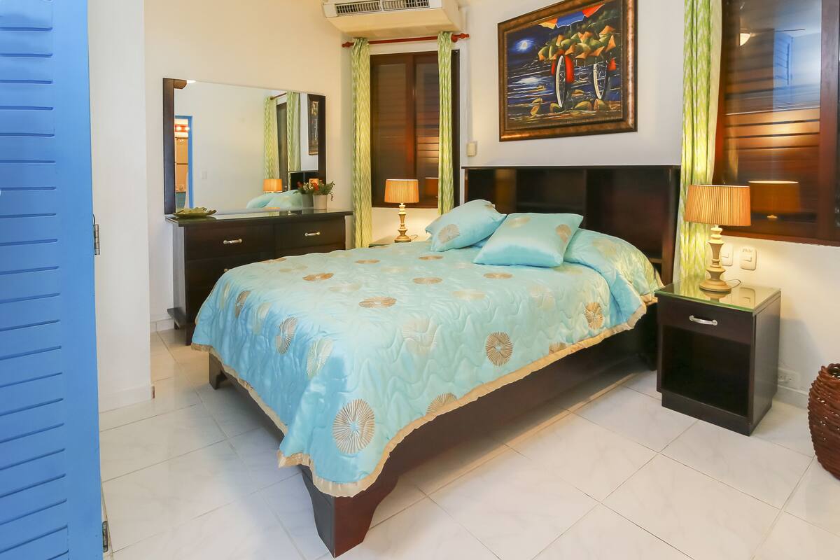 A bedroom with a bed, nightstands, a dresser, a mirror, and a painting on the wall.