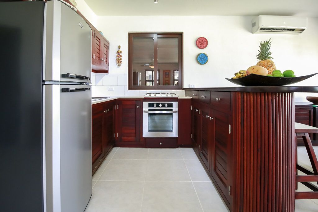 A kitchen with dark wooden cabinets, a stainless steel refrigerator, a built-in oven, and a small island with a fruit bowl.