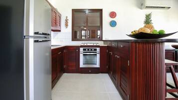 A kitchen with dark wooden cabinets, a stainless steel refrigerator, a built-in oven, and a small island with a fruit bowl.