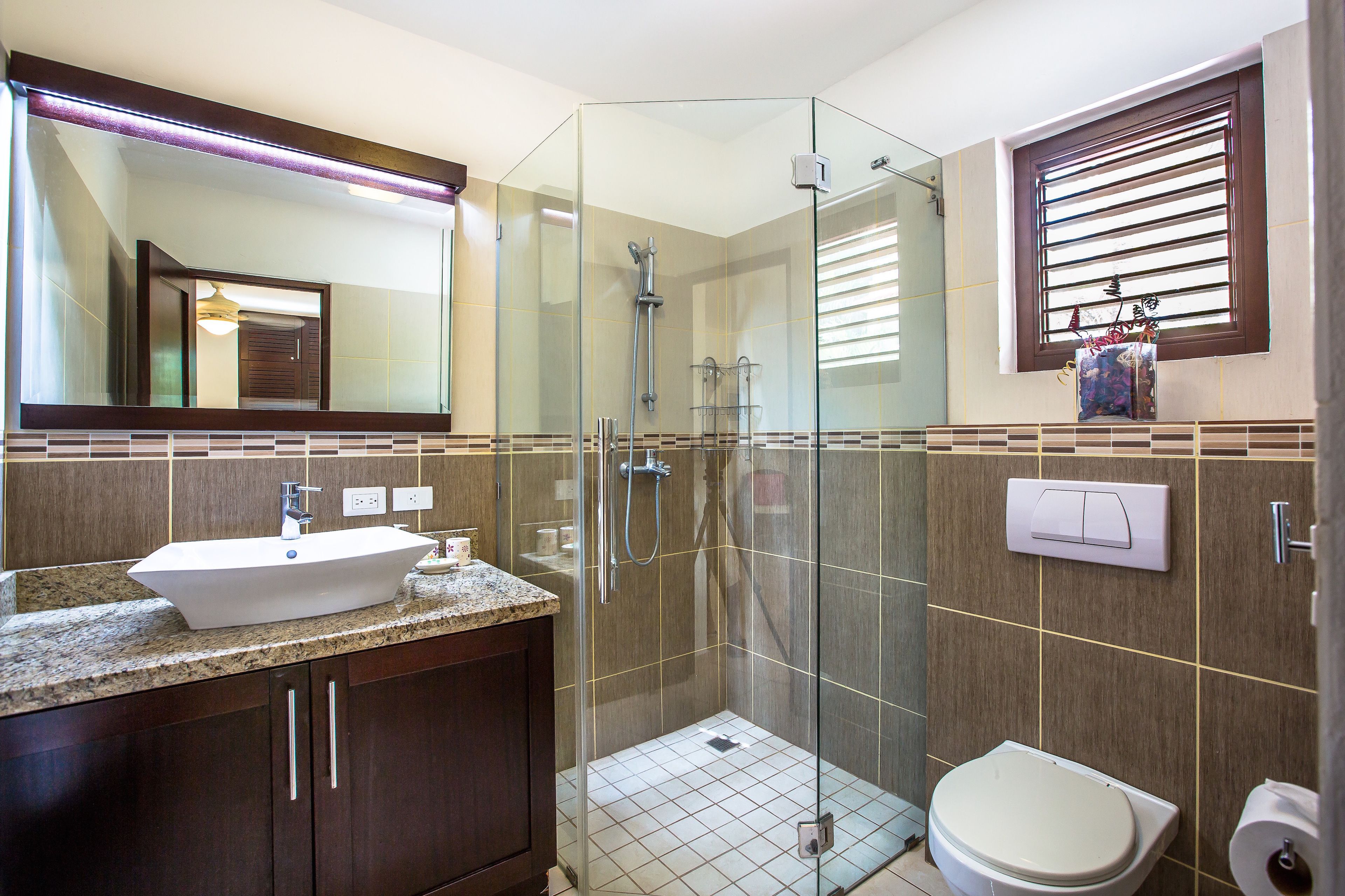 Un baño moderno con ducha de vidrio, lavamanos con encimera de mármol y retrete.