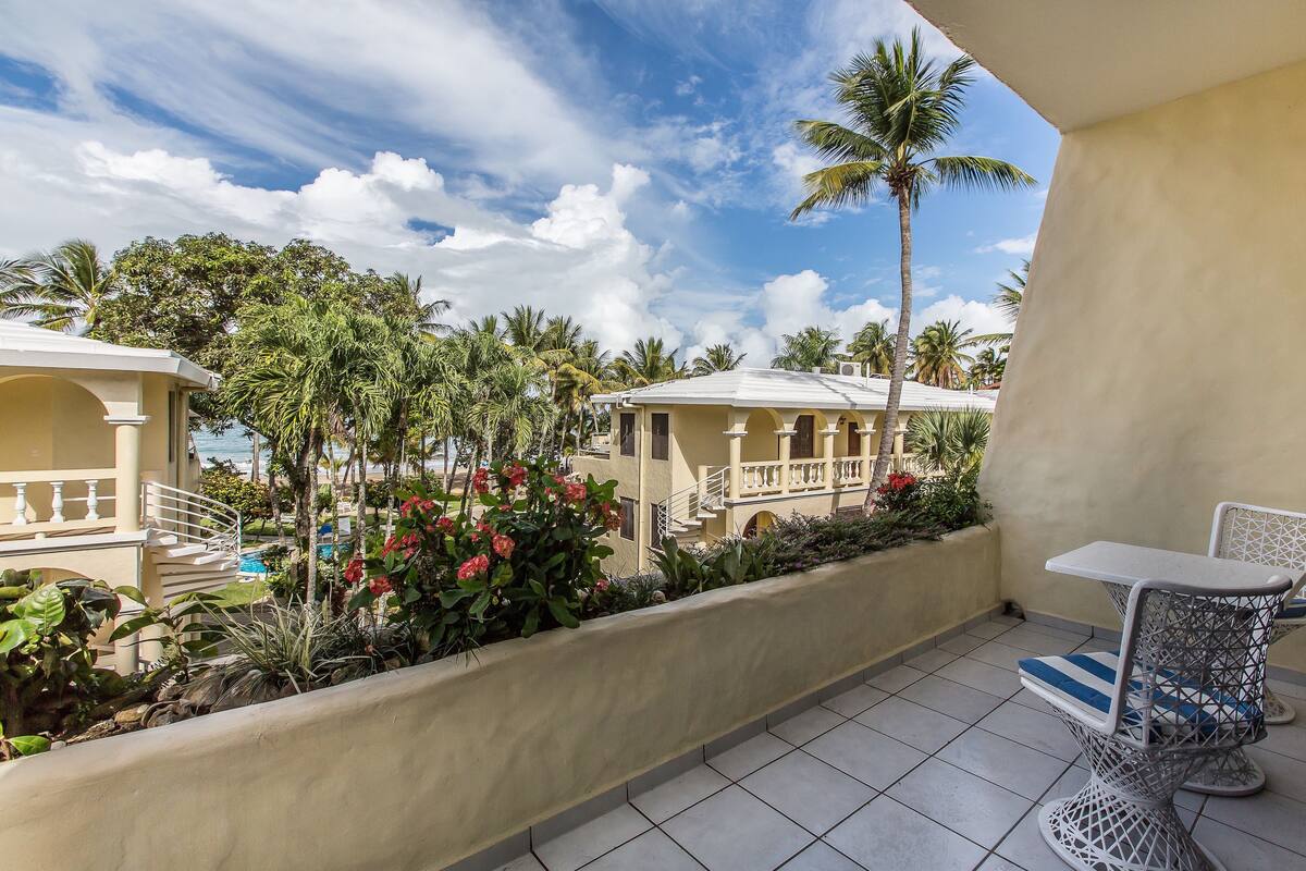 A balcony with a view of a pool, palm trees, and a building with a balcony.