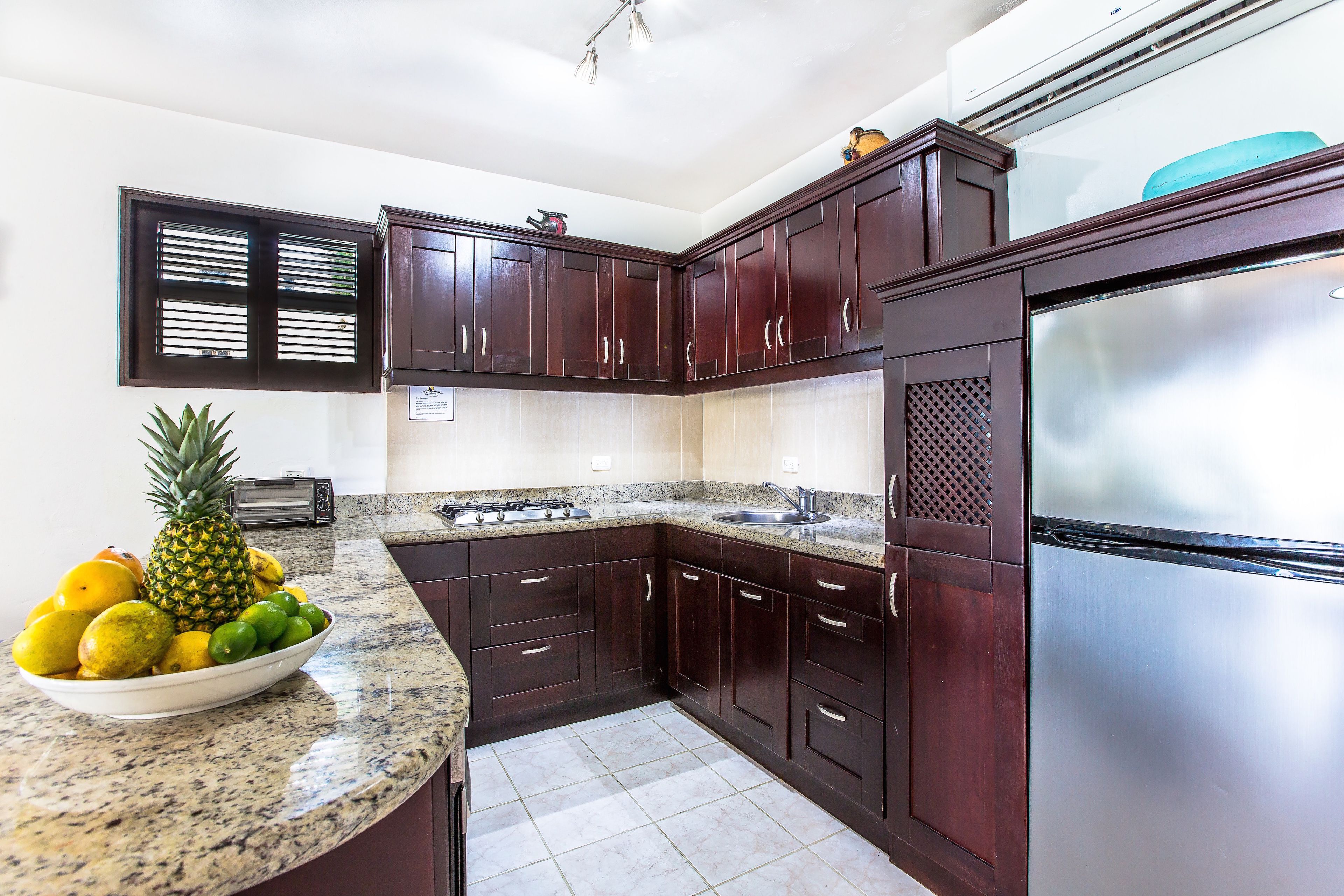 A kitchen with dark wooden cabinets, a stainless steel refrigerator, and a granite countertop.
