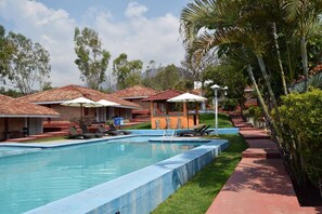 A pool area with lounge chairs and umbrellas, surrounded by buildings with red-tiled roofs and palm trees. - Hotel Chapala Country (Chapala)