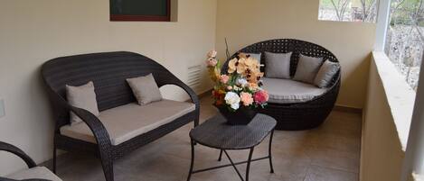 A balcony with wicker furniture, including a sofa and chairs, and a small table with a flower arrangement.