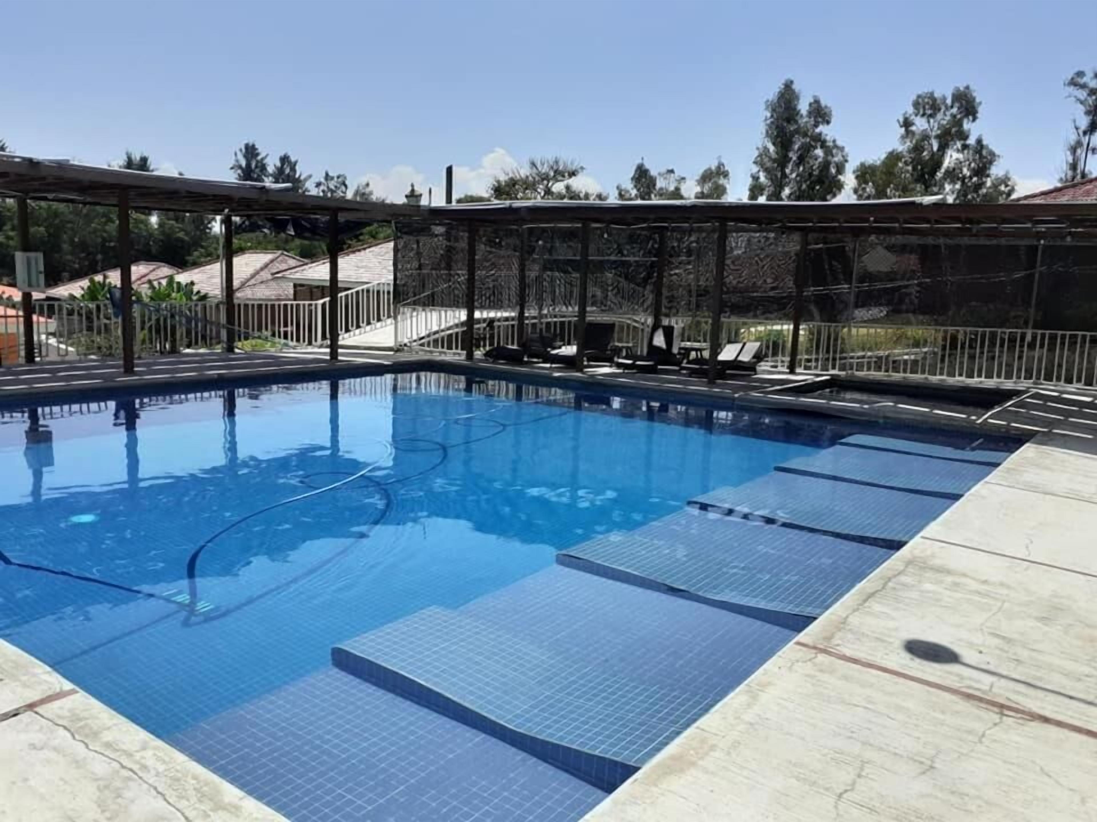 A rectangular swimming pool with clear blue water, surrounded by a metal fence.