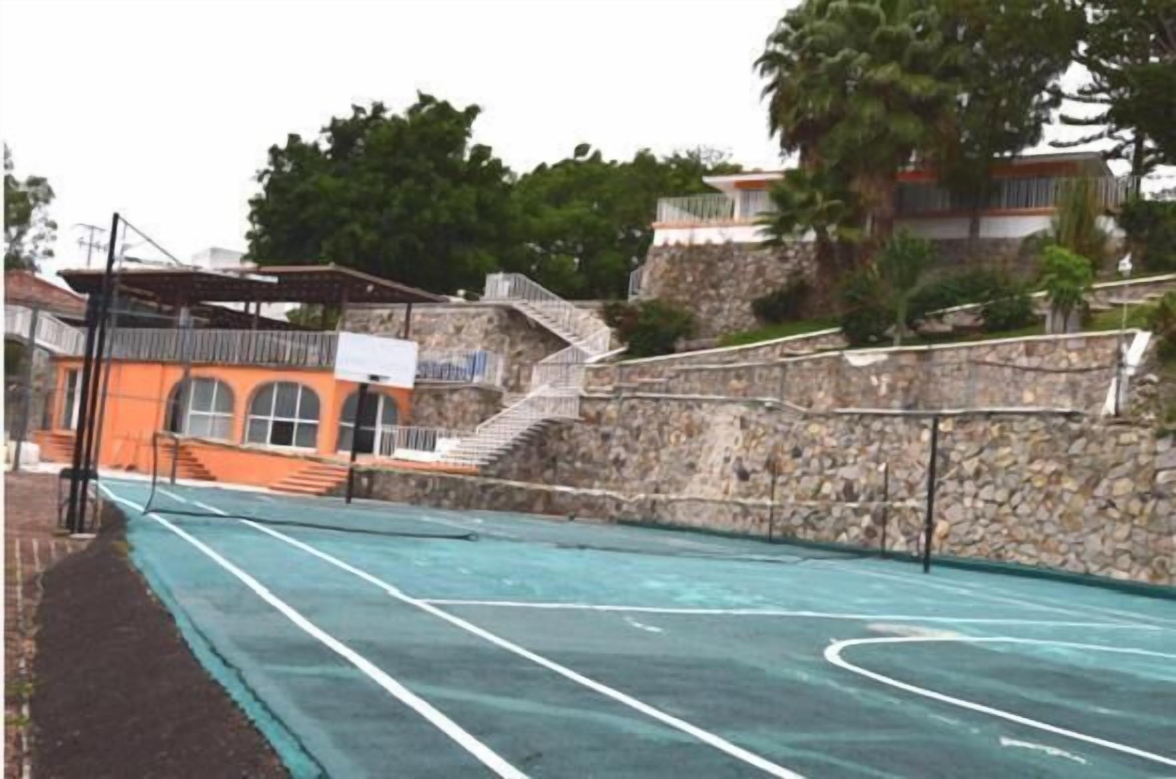 Ein Tennisplatz mit einer Steinmauer und einer Treppe, die zu einem Gebäude mit einem Balkon führt.
