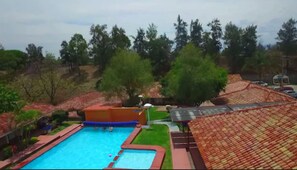 A swimming pool with a red and blue border, surrounded by green grass and trees. - Hotel Chapala Country (Chapala)