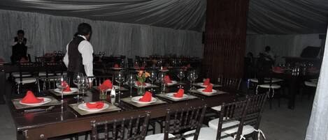 Un salón de banquetes con largas mesas dispuestas para comer, sillas de madera y un camarero atendiendo a las mesas.