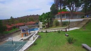 A pool area with a lifeguard stand, a small building with a red roof, and a staircase leading up to a house with a red roof.