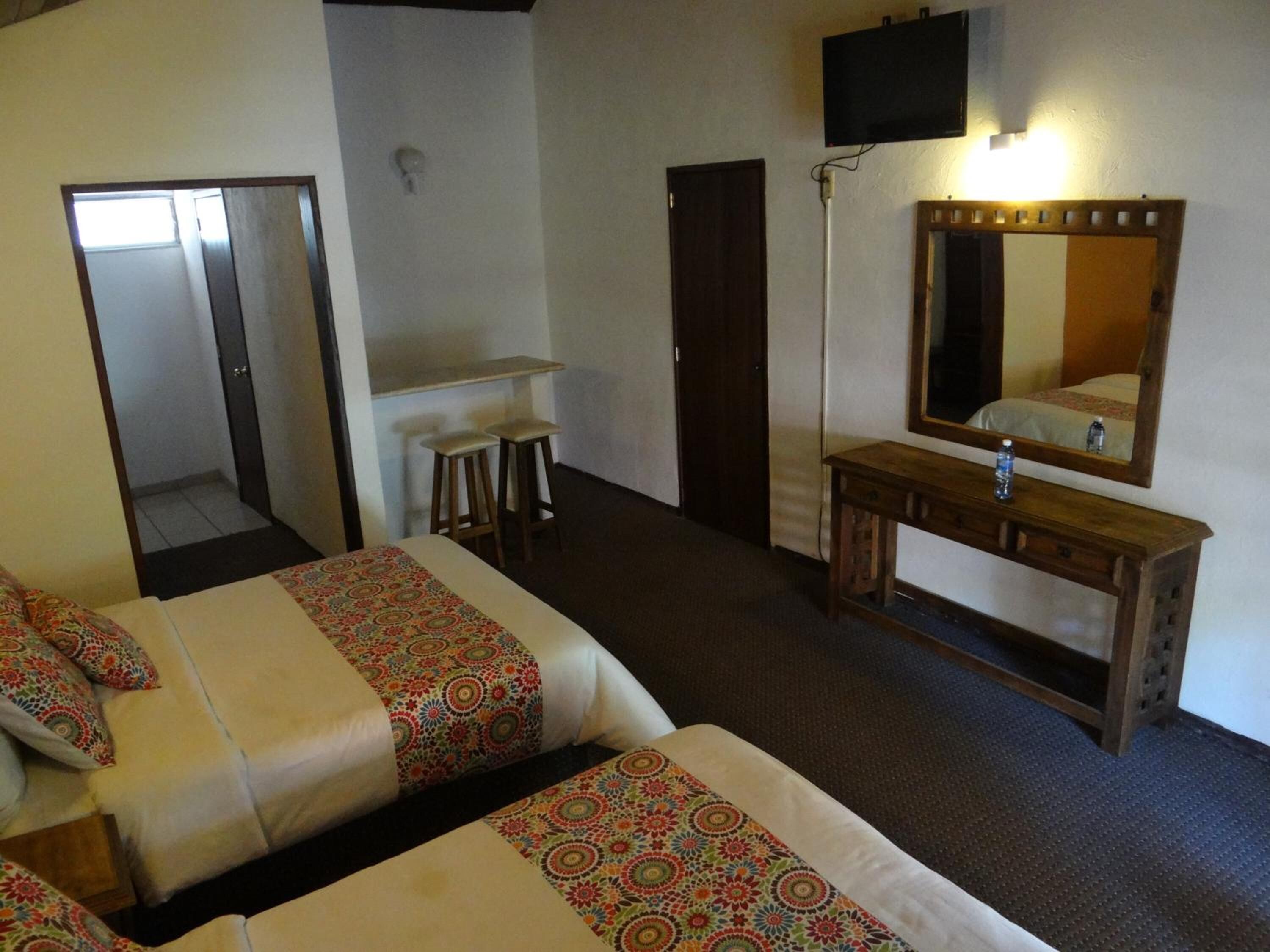 Ein Hotelzimmer mit zwei Betten, einem Holzkoffer, einem Spiegel, einem Fernseher und einem kleinen Tisch mit Hockern.