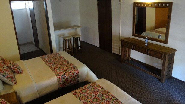A hotel room with two beds, a wooden dresser, a mirror, a television, and a small table with stools.