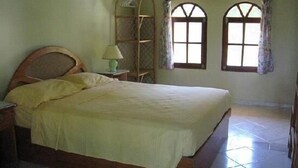 Un dormitorio con una cama de madera, una mesita de noche, una lámpara y dos ventanas con cortinas.