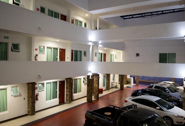 A multi-level hotel interior with several floors, a parking area with cars, and a fire extinguisher on the ground floor.