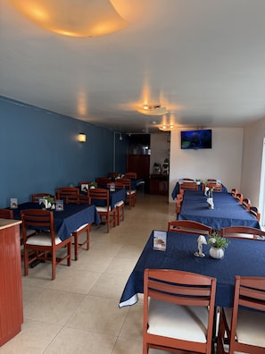 A dining area with tables set for service, chairs, and a television mounted on the wall.