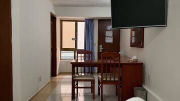 A hotel room with a bed, a desk with a chair, a television mounted on the wall, and a window with curtains.