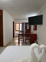 Une chambre d’hôtel comprenant un lit, un bureau avec une chaise, un téléviseur fixé au mur et une fenêtre avec des rideaux.