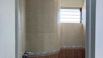 Ducha con diseño curvo, paredes de azulejos y ventana que proporciona luz natural.