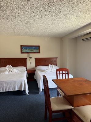 A hotel room with two beds, a wooden headboard, a painting on the wall, a wooden table, and a chair. - Hotel NV Guadalajara (Zapopan)