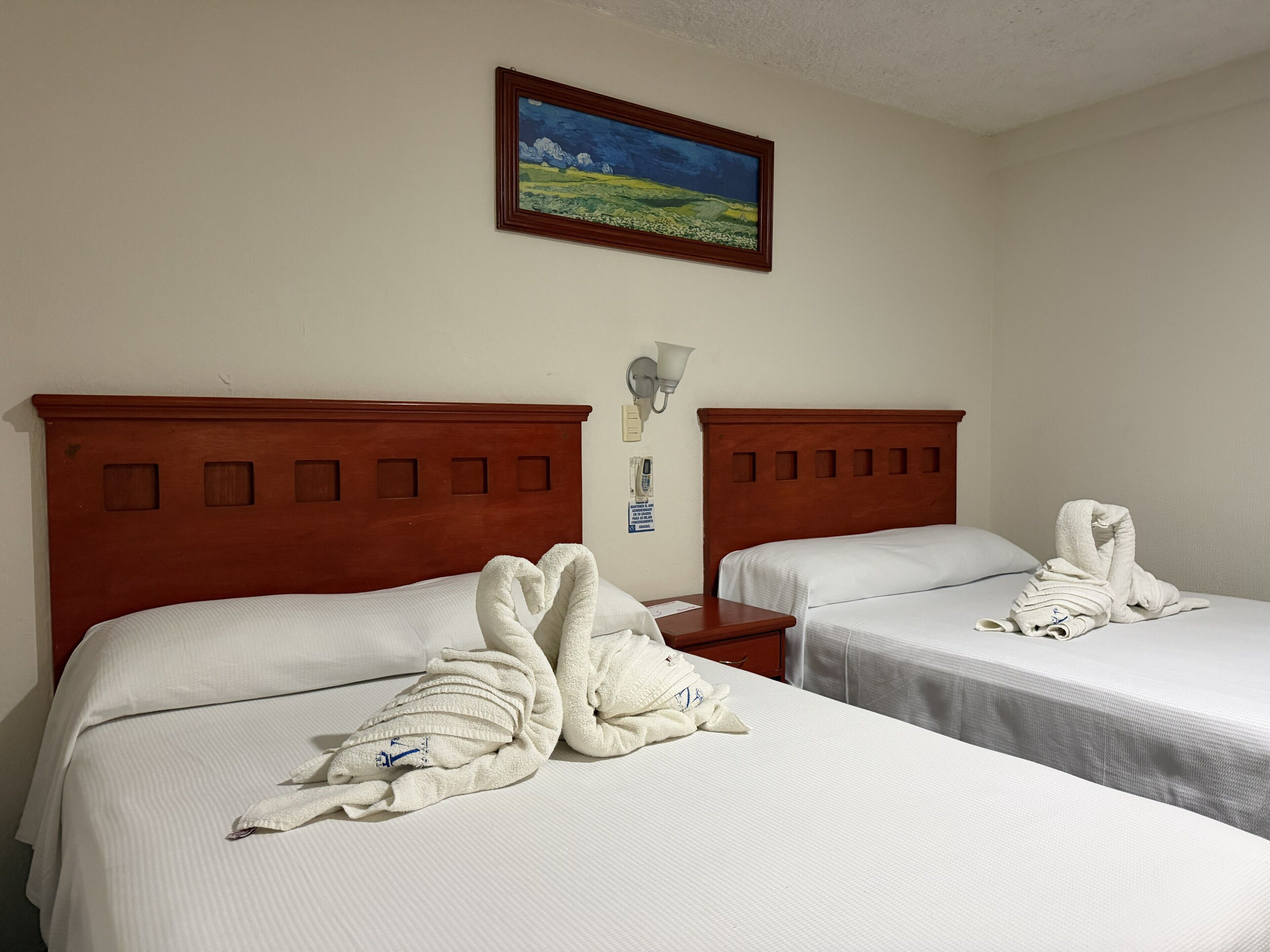Een hotelkamer met twee bedden, elk met een houten hoofdbord, witte lakens en handdoeken gerangschikt in de vorm van een hart.