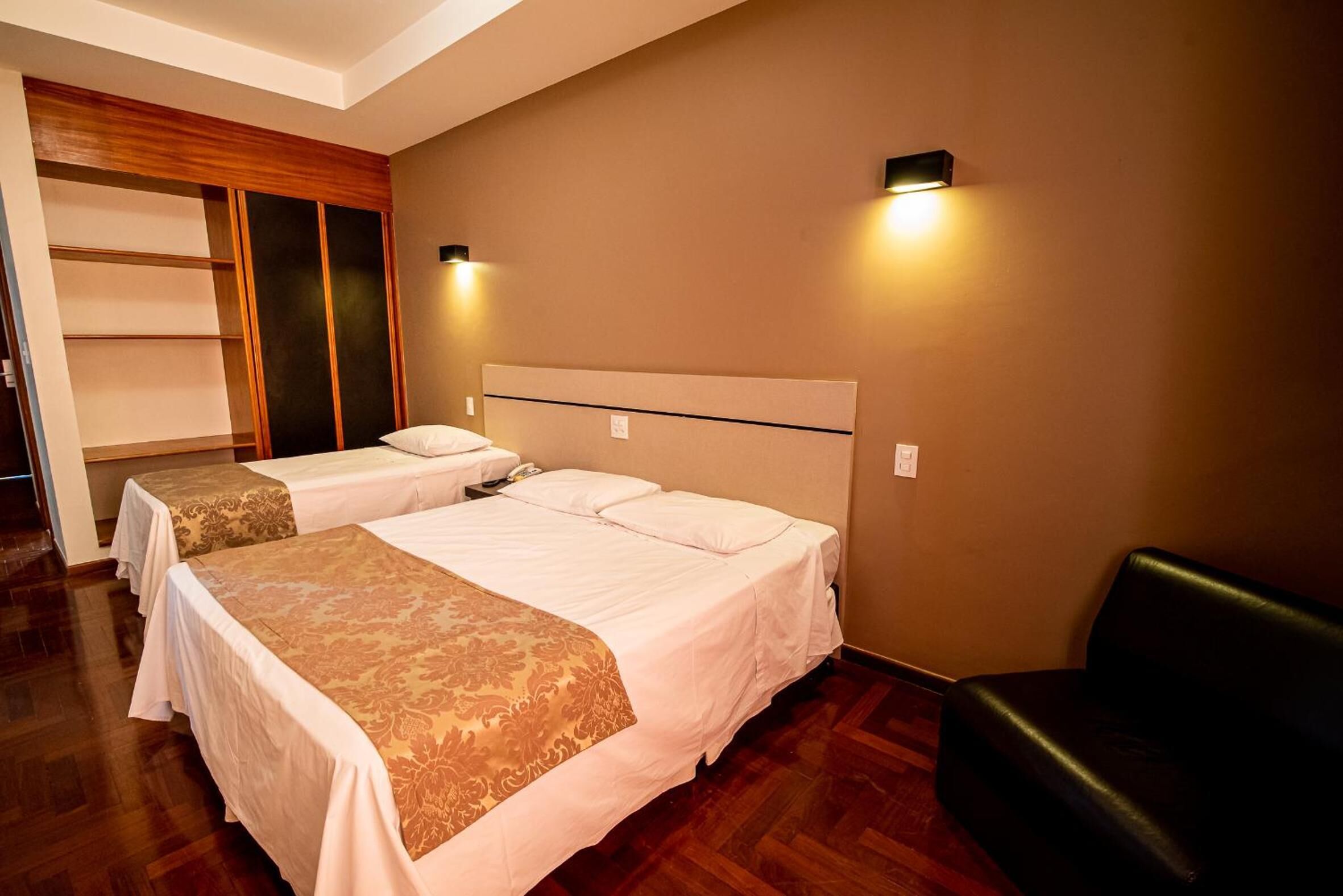 Une chambre d’hôtel avec deux lits, une armoire en bois et un canapé en cuir noir.