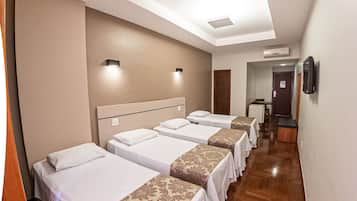 A hotel room with four beds aligned in a row, a wooden floor, and a corridor leading to a door.