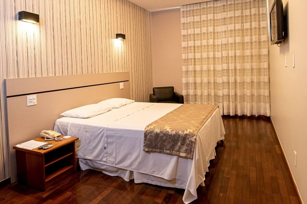 Habitación de hotel con cama, mesita de noche, lámpara y televisión en la pared.